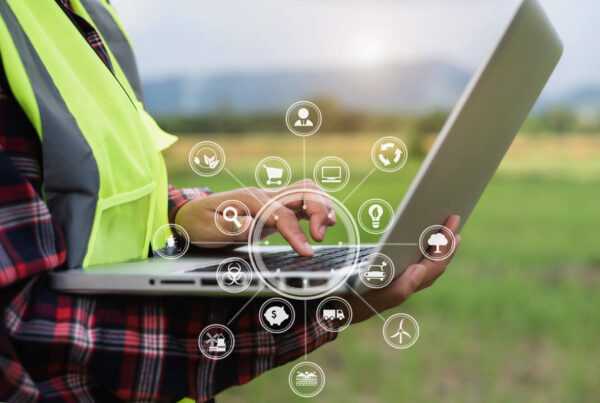 na imagem, mãos segurando um laptop prateado exibindo icones variados relacionado a tecnologia do campo
